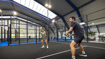 Due persone giocano una partita di padel su un campo indoor.